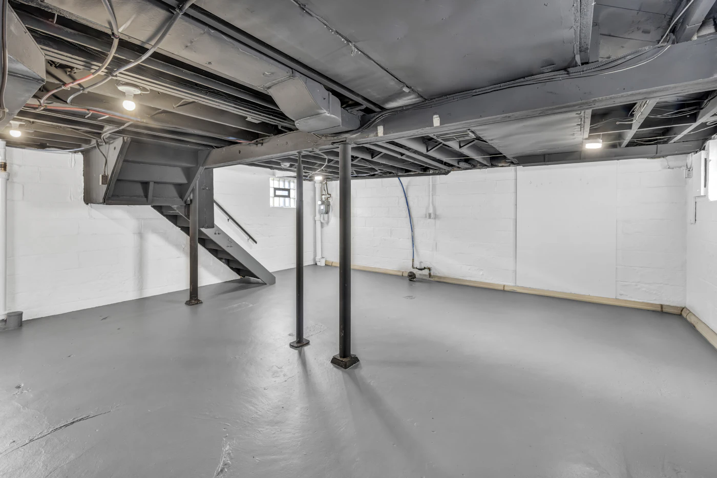 An unfinished basement with a bare concrete slab floor, exposed joists overhead and steel support posts
