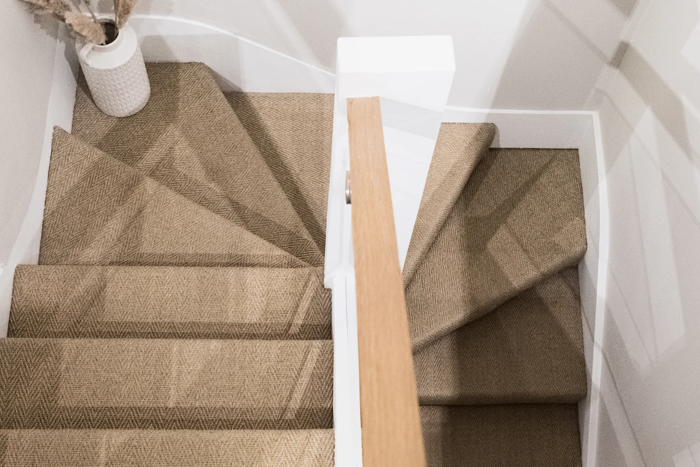 The finished staircase in hard wearing herringbone carpet, cut tight around the winders at the turn with clean white risers